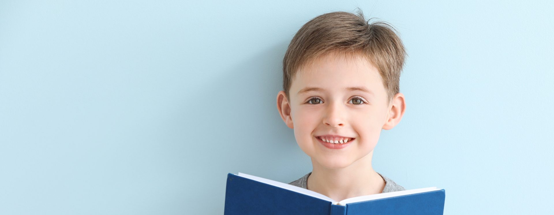 Boy smiling and reading a book with a blue cover
